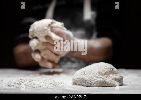 Mains de la préparation de la pâte baker mâle avec de la poussière de farine blanche sur fond noir, pour évider les pâtes et pizzas Banque D'Images