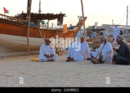 Golfe d'hommes assis sur la plage à côté d'un bateau en bois, Katara dhaw traditionnel festival, Doha, Qatar. Banque D'Images