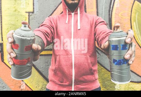 Jeune homme en train de dessiner avec deux sprays souriants - concept d'art Moderne avec un homme urbain en train de réaliser et de préparer des murales en direct avec aérosol couleur spray - Focus Banque D'Images