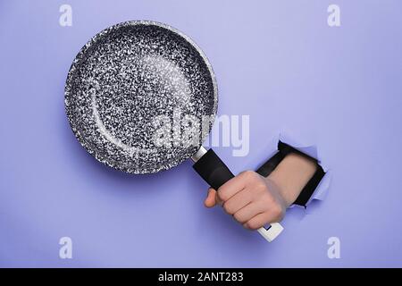 Femme méconnaissable holding poêle au moyen de papier déchiré fond violet. Des ustensiles de cuisine concept. L'espace de copie pour fins de publicité Banque D'Images