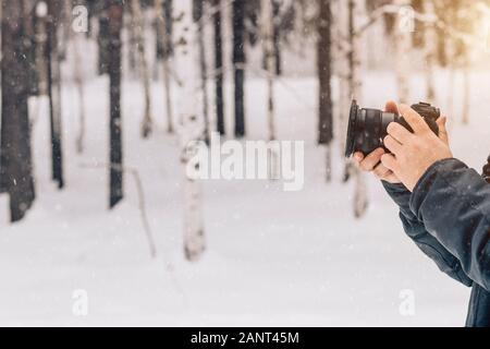 Gros plan de la main du photographe sur l'arrière-plan d'une forêt d'hiver avec des chutes de neige. Copier l'espace. L'équipement professionnel, appareil photo, stabilisateur de vid Banque D'Images