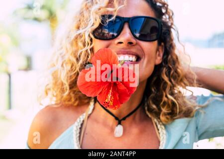 Printemps et de bonheur concept avec happy cheerful dame de prendre une grande fleur rouge avec des dents dans la bouche de sourire et de jouer en face de l'appareil photo - bea Banque D'Images