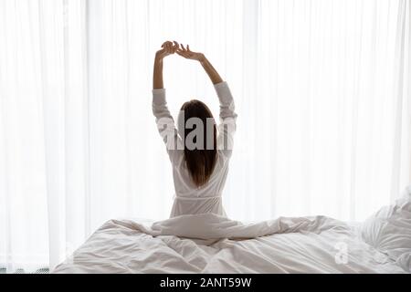 Beautiful woman sitting on bed, stretching arms le matin Banque D'Images