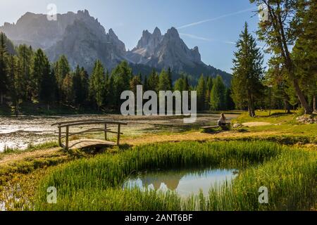 Fille assise dans un lac idyllique dans les Dolomites Sexten entouré de forêts de pins, Lago d'Antorno, province de Belluno, Dolomites Sexten, Italie Banque D'Images