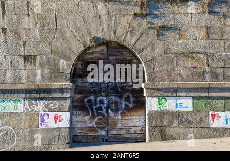 Close-up de la porte en bois d'un vieux hangar à bateaux sur la banque du fleuve Po (Murazzi) avec des pochoirs de graffiti sur le mur de pierre, Turin, Piémont, Italie Banque D'Images