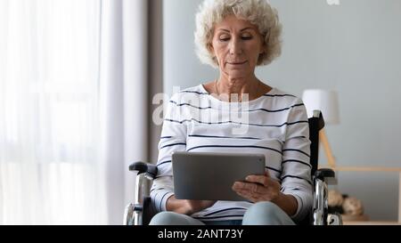 Vieille Femme assise dans un fauteuil roulant, à l'aide d'ordinateur Tablet Banque D'Images