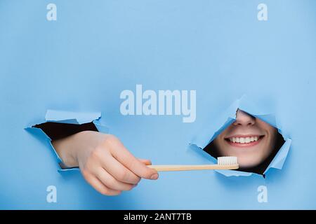 Femme avec dents agréable sourire sur le visage, la tête et le bambou eco permet grâce à la brosse à dents dans le trou déchiré papier bleu, copie de l'espace pour votre promotion. Dental Banque D'Images