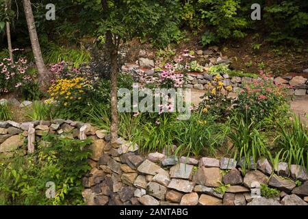 Bordure en pierre surélevée avec Rudbeckias jaune et Purple Echinacea purpurea - Coneflowers dans jardin privé de campagne en été Banque D'Images