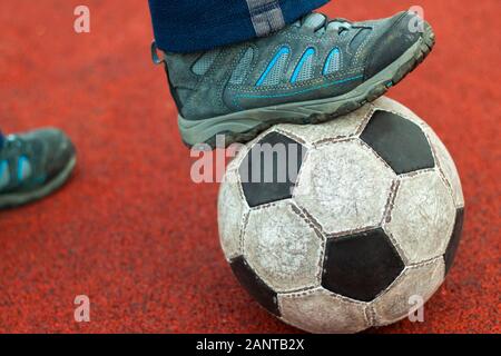 Pied humain dans une sneaker sale sur un vieux ballon de football. Banque D'Images