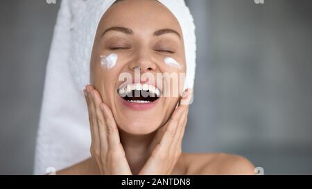 Close up heureux belle femme en riant, l'application de crème hydratante Banque D'Images