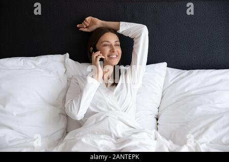 Smiling Beautiful Woman talking on phone, sitting in bed Banque D'Images