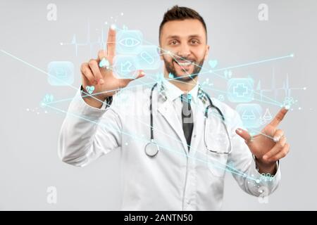 Portrait du médecin souriant avec strethoscope sur le cou portant un manteau de laboratoire. Mise au point sélective de l'écran des cartes tactiles numériques, homme touchant des icônes virtuelles sur la projection. Concept de numérisation, médecine. Banque D'Images