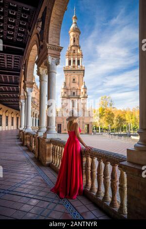 Séville / Espagne - 29 novembre 2019 : La femme blonde en robe rouge et avec le chapeau est à regarder l'historique de l'Espagne (carrés enchanteresse Plaza de España). Banque D'Images