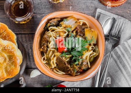 L'ouzbek et nouilles asiatiques traditionnelles lagman avec les légumes et la viande sur la table en bois rustique, d'arrière-plan. Vue d'en haut Banque D'Images