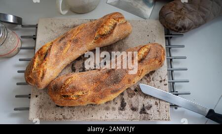 Vue du dessus du four de deux baguettes au levain fait maison sur une pierre de refroidissement sur le comptoir de la cuisine. Banque D'Images