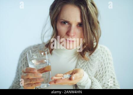 Portrait de malades concernés 40 ans femme moderne rouleau à col roulé et veste avec tasse de l'eau tenant un grand nombre de pilules sur winter light blue backg Banque D'Images