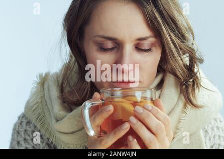 Joyeux malades d'âge moyen élégant femme en roll col roulé et veste de boire tasse de thé au gingembre, citron et miel isolé sur la lumière d'hiver Banque D'Images