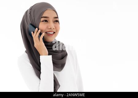 Portrait of attractive asian young adult femme musulmane dans un hijab blanc talking on mobile phone isolé sur fond blanc. En utilisant la technologie pour un Banque D'Images