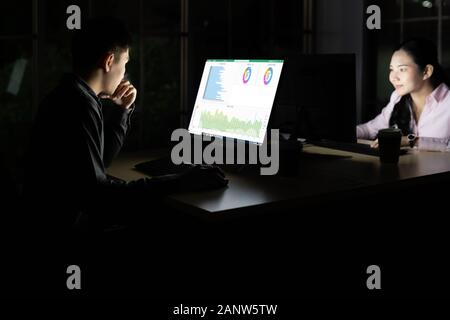 Young adult asian businessman and woman travailler tard dans la nuit dans leur bureau avec ordinateur de bureau et ordinateur portable. En utilisant comme travail dur et travailler tard Banque D'Images