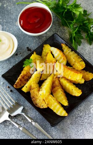 Le fast food. Les pommes de terre cuites au four avec des épices, des tranches sur l'ardoise ou la pierre, servi avec de la mayonnaise et du ketchup sauce. Banque D'Images