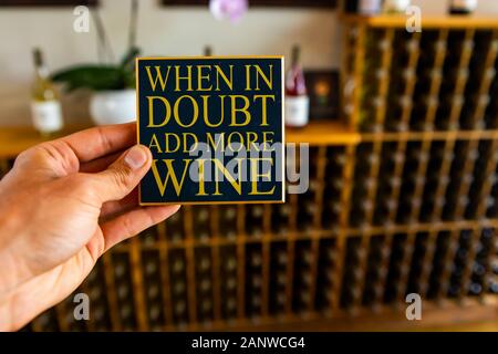 En cas de doute ajouter plus de vin, main tenant un devis signer selective focus, une salle de dégustation boutique intérieur, bouteilles de vins en bois sur fond de rack Banque D'Images