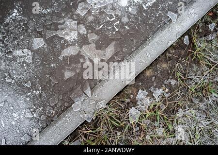 Flaque d'eau gelée avec des morceaux de glace, pelouse sèche couverte de givre et en divisant leur trottoir de l'hiver, un jour de grand froid. Banque D'Images