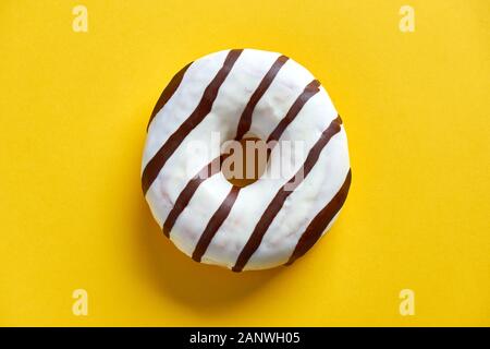Un seul anneau rond avec vitrage sur glace blanche et rayures de chocolat brun foncé sur fond jaune avec espace de copie. Pose plate. Banque D'Images