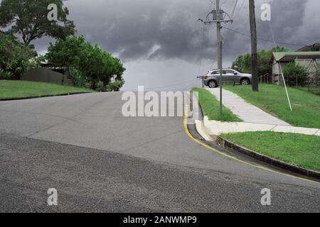 Un ciel gris spectaculaire de nuages de pluie d'un angle bas sur une rue de banlieue, route grise, herbe vert vif, arbres, sentier en béton blanc, Australie, banlieue Banque D'Images