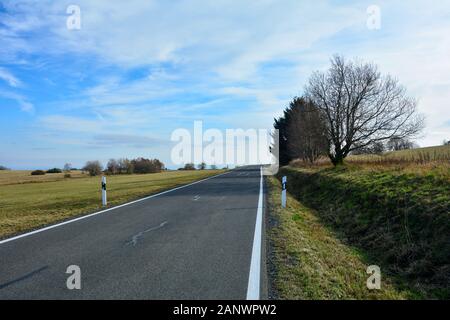 Route solitaire à travers un paysage verdoyant, avec ciel bleu, les arbres sur le côté droit, dans le Rhoen, Bavière, Allemagne Banque D'Images