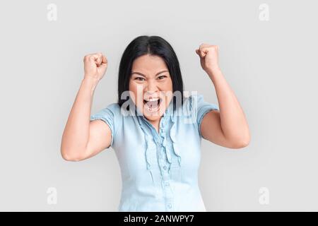 Freestyle. Asian woman isolated on white mains en poings, hurlant à huis clos et l'expression émotionnelle Banque D'Images