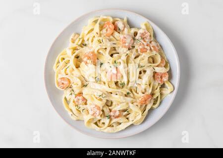 Les pâtes italiennes ou tagliatelle fettuccine dans une sauce crémeuse aux crevettes dans une assiette sur la table en marbre blanc Vue de dessus. Banque D'Images