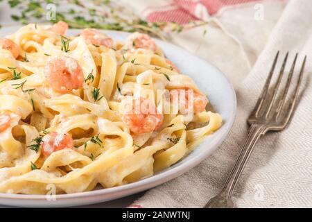 Les pâtes italiennes ou tagliatelle fettuccine aux crevettes dans une sauce crémeuse au parmesan et thym dans une assiette sur la table en marbre blanc. close up Banque D'Images