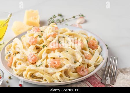 Les pâtes italiennes Les fettuccine aux crevettes dans une sauce crémeuse au parmesan et thym dans une assiette sur la table en marbre blanc. close up Banque D'Images