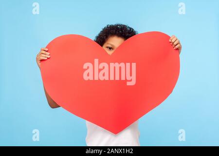 Cute adorable petit garçon timide, à big red paper heart, méconnaissable enfant tenant symbole de l'amour, la charité, à la recherche, avec l'intérêt est venu Banque D'Images