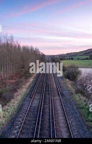 Des voies ferrées droites se dirigeant à la distance au coucher du soleil entouré par La Campagne anglaise Banque D'Images
