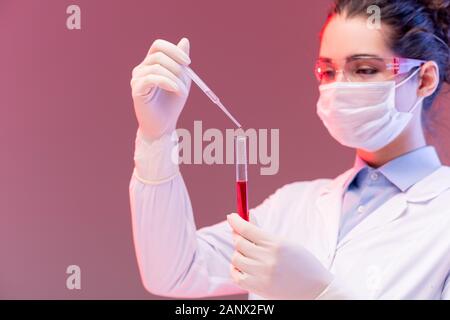 Jeune chimiste en lunettes de protection et masque l'abandon dans la fiole de liquide rouge Banque D'Images