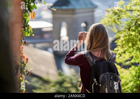 Jeune femme séduisante debout en arrière avec un sac à dos prenant une photo de la vieille région de Salzbourg avec le coucher de soleil. Concept de voyage. Banque D'Images