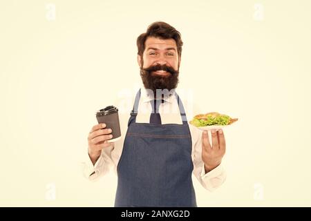 Cafe food concept. Homme garçon barbu tablier porter porter la plaque avec la nourriture et tasse à café. Profitez de votre repas. Guy servant un croissant fourré la laitue et les légumes frais. Alimentation saine. De délicieux croissants. Banque D'Images