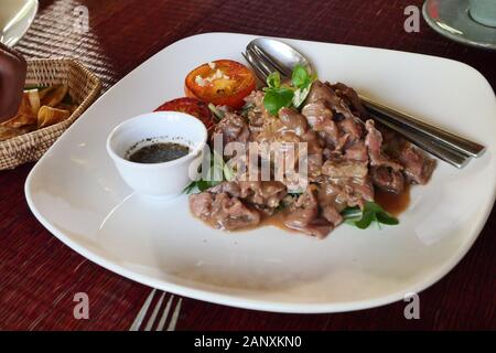 Saveur boeuf mariné frit cambodgien(( Lok Lak ) avec des tranches de tomate en plaque blanche sur table rouge Banque D'Images