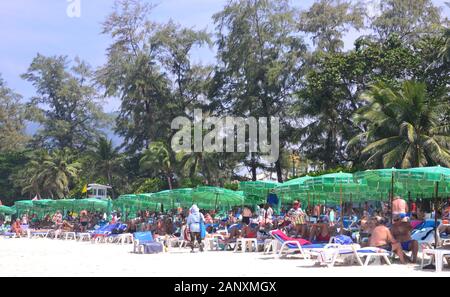 Touristes sous les parasols verts profitez de la plage et mer à Patong Beach, Phuket, Thaïlande, Asie, par une chaude journée avec un ciel bleu Banque D'Images