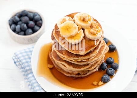 Des crêpes au banane, myrtille, sirop de caramel et noix concassées sur une plaque blanche, vue rapprochée. Délicieux petit déjeuner d'un doux Banque D'Images