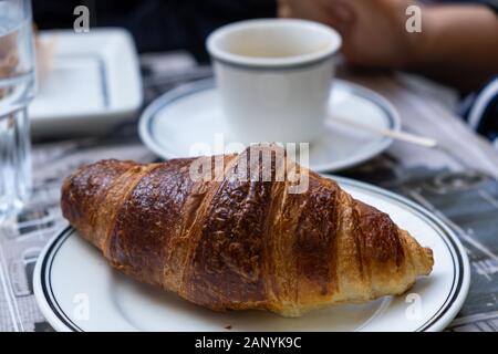Café et croissant. Un bien-fait croissant au beurre sur un plat blanc en vue rapprochée. Coupe du flou sur l'arrière-plan d'une soucoupe. Banque D'Images