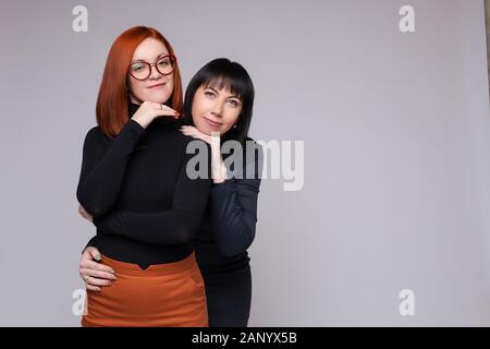 Deux femmes adultes smiling at camera. Dark-haired woman embracing son amie par derrière. Banque D'Images
