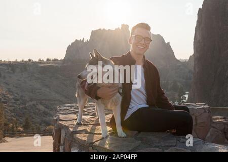 Un jeune homme avec son chien husky jouit du coucher du soleil à Smith Rock State Park Banque D'Images