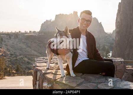 Un jeune homme avec son chien husky jouit du coucher du soleil à Smith Rock State Park Banque D'Images