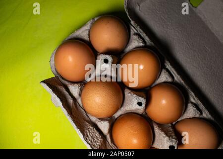 Les oeufs de poule dans une boîte, sur un fond jaune, tourné à partir de ci-dessus, en attente d'être mangés Banque D'Images