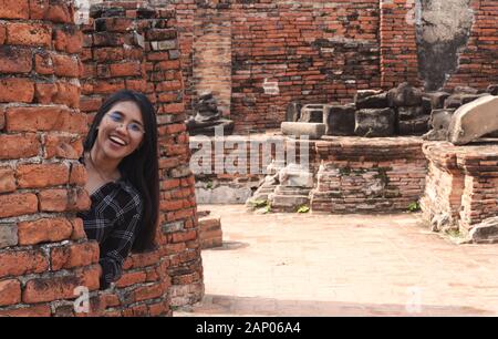 Jeune fille asiatique amusante et variée se cachant derrière un mur de briques et souriant - influenceur social hipster millénaire se rendant aux destinations touristiques culturelles - concept de voyage, tendances et idées de vacances Banque D'Images