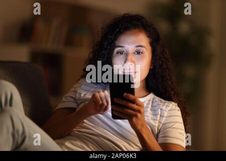 Femme sérieuse dans la nuit à l'aide de smart phone assis sur un canapé dans la salle de séjour à la maison Banque D'Images