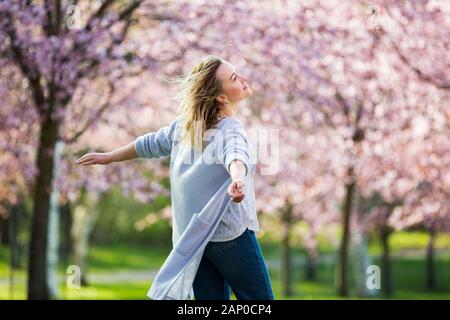 Jeune femme profitant de la nature au printemps. Danse, course à pied et tourbillon dans un beau parc avec des cerisiers en fleurs. Concept de bonheur Banque D'Images
