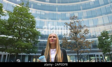 Par en dessous de la blonde woman in suit le café dans la tasse de papier à l'écart sur rue. Banque D'Images